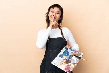 Arkaplanda palet tutan genç bir sanatçı sessizlik hareketi yapıyor.