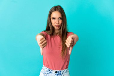 İzole edilmiş mavi arka planda genç bir kadın baş parmağını iki eliyle aşağı gösteriyor.