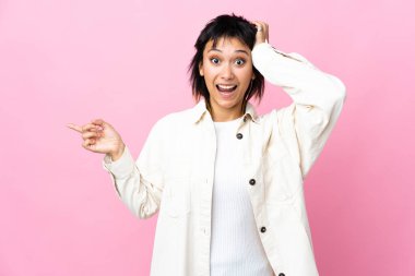 Genç Uruguaylı kadın soyutlanmış pembe arka planda şaşırmış ve parmağıyla kenarı işaret ediyor.