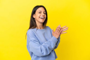 Sarı arka planda izole edilmiş genç beyaz kadın alkışlıyor.