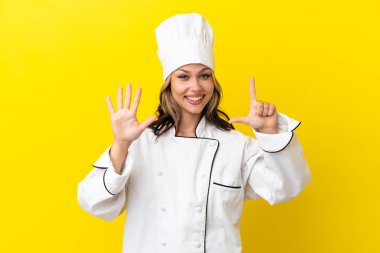 Sarı arka planda izole edilmiş genç Rus şef kız parmaklarıyla yediyi sayıyor