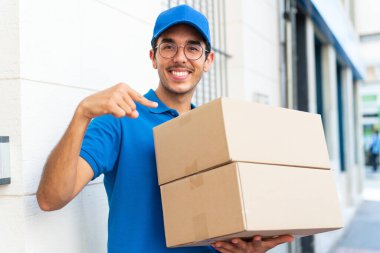 Genç teslimatçı dışarıda kutuları tutuyor ve kutuları işaret ediyor.