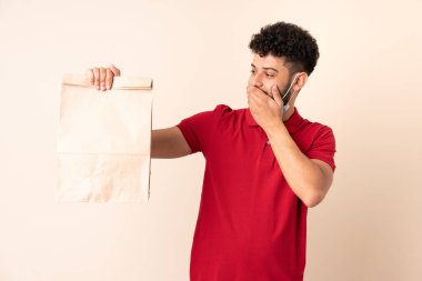 Elinde yemek çantası tutan genç bir adam. Şaşırmış ve şok olmuş bir yüz ifadesi var.