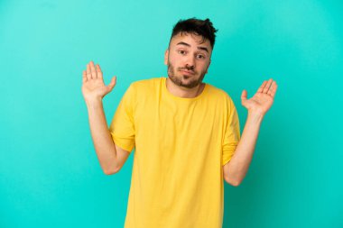 Mavi arka planda izole edilmiş genç beyaz adam şüpheli hareketler yapıyor.