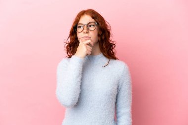 Pembe arka planda izole edilmiş genç kızılımsı kadının şüpheleri ve düşünceleri var.
