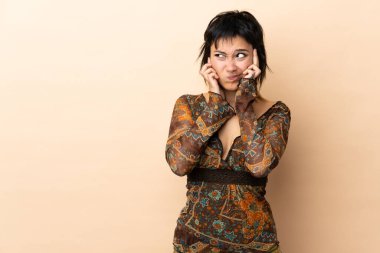 Bej arka planda izole edilmiş Hintli kadın hayal kırıklığına uğramış ve kulaklarını kapatmış.