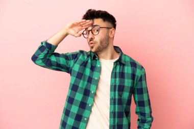 Pembe arka planda izole edilmiş genç beyaz adam yan tarafa bakarken sürpriz jest yapıyor.