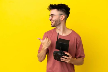 Elinde uzaktan kumanda tutan adam sarı arka planda izole edilmiş bir ürün sunmak için yan tarafı işaret ediyor.