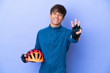 Mor arka planda izole edilmiş genç beyaz adam mutlu ve parmaklarıyla üçe kadar sayıyor.