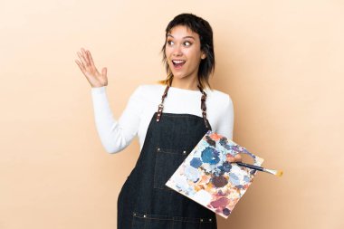 Arkaplanda palet tutan genç bir sanatçı sürpriz bir yüz ifadesiyle.