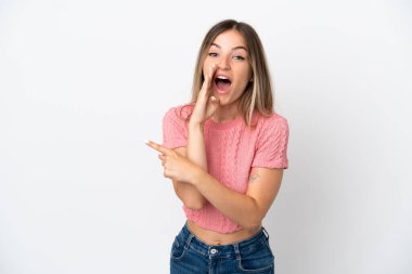 Beyaz arka planda izole edilmiş genç Romen kadın bir ürün sunmak ve bir şeyler fısıldamak için kenarı işaret ediyor