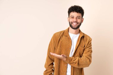 Bej arka planda izole edilmiş genç Faslı bir adam gülümserken bir fikir sunuyor.