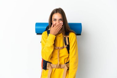 Genç dağcı kadın, izole edilmiş beyaz arka planda büyük bir sırt çantasıyla mutlu ve gülümseyen elleriyle ağzını kapatıyor.