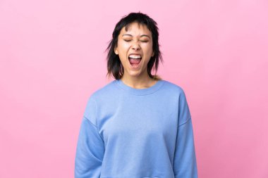 Genç Uruguaylı kadın, pembe arka planda, ağzı açık bağırıyor.