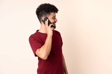 Bej arka planda izole edilmiş genç Faslı bir adam cep telefonuyla sohbet ediyor.