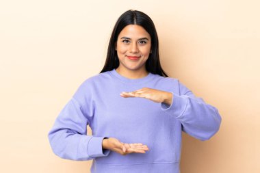 İzole edilmiş arka planda kalan genç Latin kadın bir ilan vermek için avucunun içinde hayali bir şey tutuyor.