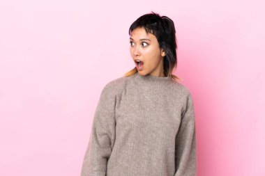Genç Uruguaylı kadın pembe arka planda, yan tarafa bakarken sürpriz jest yapıyor.