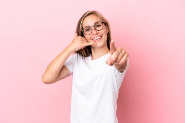 Pembe arka planda izole edilmiş genç bir İngiliz kadın telefon jesti yapıyor ve ön tarafı işaret ediyor.