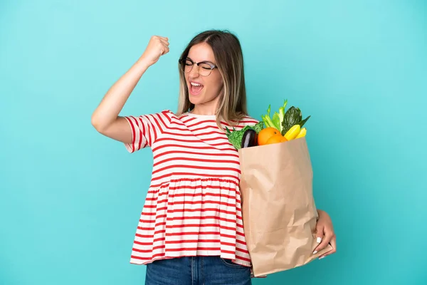 Young Woman Holding Grocery Shopping Bag Isolated Blue Background Celebrating — Stock Photo, Image