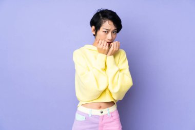 Kısa saçlı genç Vietnamlı kadın mor arka planda gergin ve korkmuş bir şekilde elleriyle suni teneffüs yapıyor.