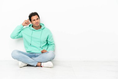 Kafkasyalı yakışıklı bir adam yerde oturuyor şüpheleri var ve kafası karışmış bir yüz ifadesi var.