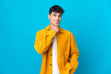 Soyutlanmış mavi arka planda genç bir adam yana bakıyor ve gülümsüyor.