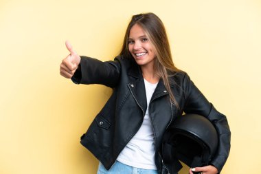 Sarı arka planda izole edilmiş motosiklet kasklı beyaz bir kadın baş parmak işareti yapıyor.