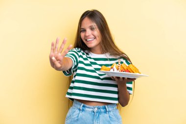 Sarı arka planda gözleme tutan genç beyaz kadın mutlu ve parmakları olan dört kişi sayıyor.