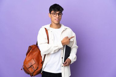 İzole edilmiş mor arka planda genç bir öğrenci parmak işareti yapıyor.