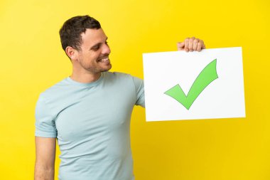 İzole edilmiş mor arkaplan üzerinde Brezilyalı bir adam elinde mutlu ifade ile yeşil onay işareti simgesi olan bir pankart tutuyor