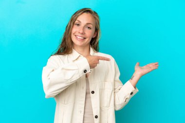 Mavi arka planda izole edilmiş genç beyaz kadın bir ilan vermek için avucunun içinde hayali bir fotokopi makinesi tutuyor.