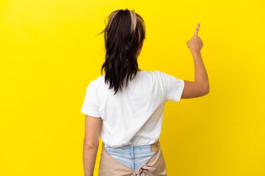 Restoran garsonu Rus kız sarı arka planda izole edilmiş işaret parmağıyla işaret ediyor.