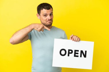 Mor arkaplan üzerinde Brezilyalı bir adam açık yazılı bir pankart tutuyor ve onu işaret ediyor.