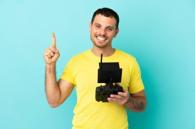 Brezilyalı bir adam uzaktan kumandayla izole edilmiş mavi arkaplanı kontrol ediyor ve en iyinin işaretini veriyor.