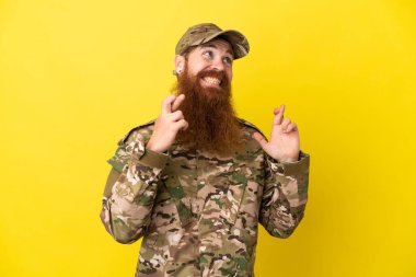 Askeri kızıl saçlı adam sarı arka planda izole edilmiş ve şans diliyor.