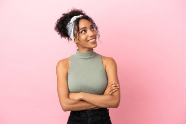 Genç Latin kadın pembe arka planda izole edilmiş gülümserken yukarı bakıyor