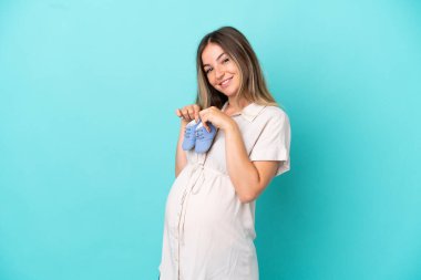 Genç Romen kadın mavi arka planda izole edilmiş hamile ve bebek poposu tutuyor