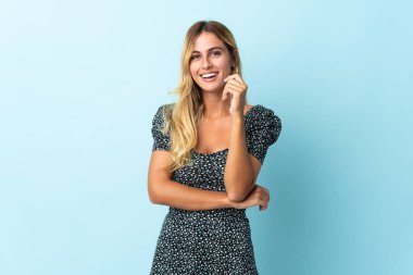 Genç sarışın Uruguaylı, mavi arka planda tek başına gülüyor.