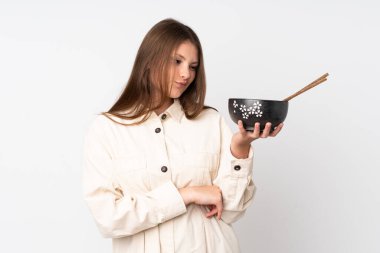 Beyaz arka planda, elinde çubuklarla elinde bir kase şehriye tutarken üzgün bir ifadeyle izole edilmiş beyaz bir kız.