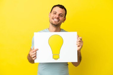 İzole edilmiş mor arka plan üzerinde Brezilyalı bir adam elinde mutlu ifadeli bir ampul simgesi olan bir levha tutuyor.