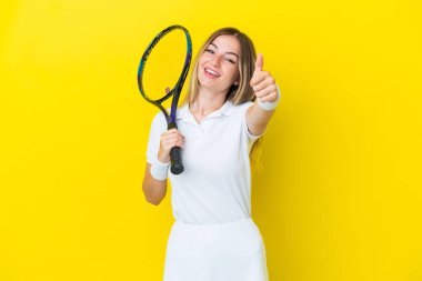 Genç Romen kadın sarı arka planda izole edilmiş tenis oynuyor ve başparmağı havada