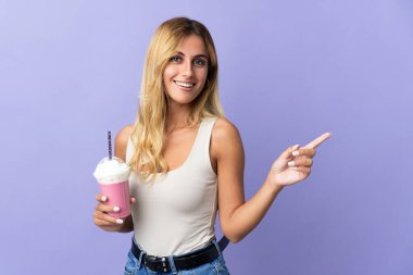 Çilekli milkshake 'li genç sarışın kadın mor arka planda izole edilmiş ve parmağını kaldırıyor.