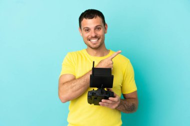 İzole edilmiş mavi arkaplan üzerinde uzaktan kumanda tutan Brezilyalı bir adam bir ürünü sunmak için yan tarafı işaret ediyor