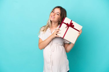 Genç Romen kadın mavi arka planda izole edilmiş hamile ve elinde bir hediye var