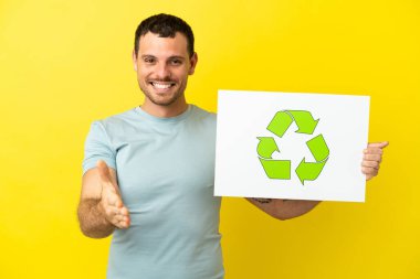 Mor arka planda kalan Brezilyalı adam elinde geri dönüşüm simgesiyle bir pankart tutuyor ve anlaşma yapıyor.