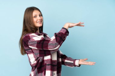 Kafkasyalı genç bir kız mavi arka planda izole edilmiş bir ilan vermek için kopyalama alanı tutuyor.