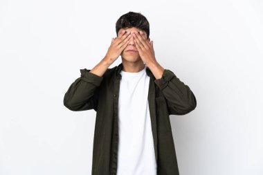İzole edilmiş beyaz arka planı olan genç bir adam elleriyle gözlerini kapatıyor.