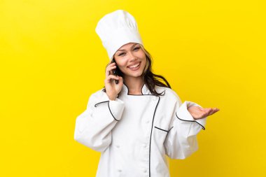 Sarı arka planda izole edilmiş genç bir Rus şef kız cep telefonuyla sohbet ediyor.