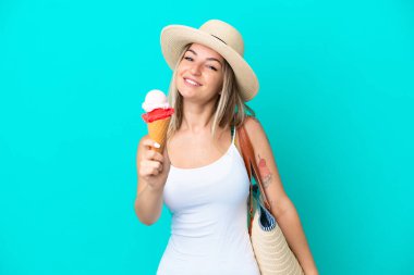 Elinde dondurma ve plaj çantası tutan genç Romen kadın mavi arka planda neşeli bir ifadeyle izole edilmiş