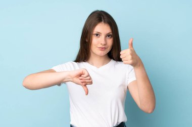 Beyaz kız mavi arka planda izole edilmiş, iyiye kötüye işaret yapıyor. Evet ya da hayır arasında kararsız